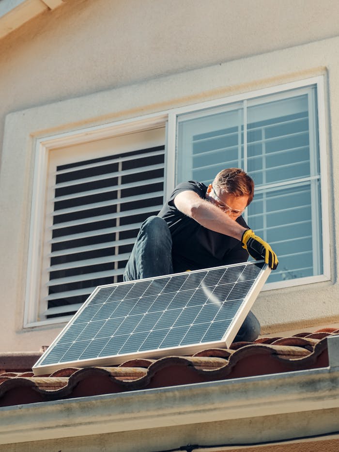 gallery-1 Man installing a solar panel on a residential rooftop, promoting sustainable energy.